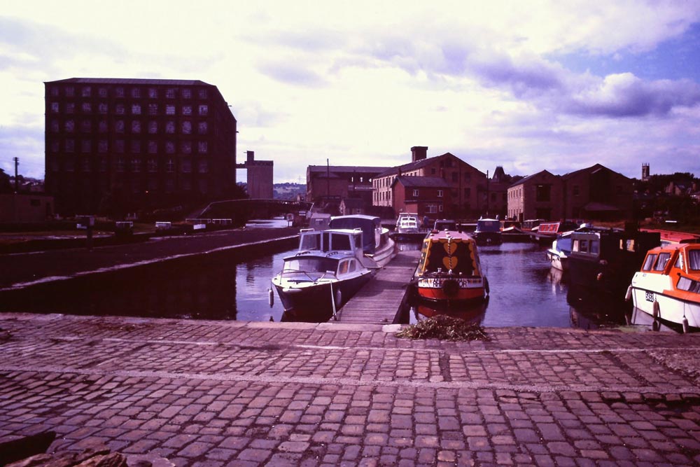 A 1980 blue sky white clouds summer day view, looking west from Karens Day, of the Calder and Hebble Navigation Canal Basin Marina, with many leisure boats, towards the former Millroyd Mill and now demolished Victoria Mill Complex, Brighouse, Calderdale, West Yorkshire, UK