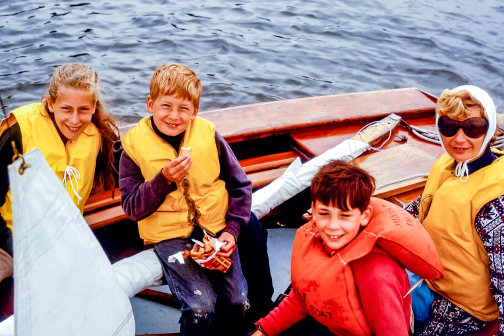 Family of a woman and three children wearing life vests in a small sailing boat on the Helford River, Cornwall, England, UK in the 1960s. Digital conversion of archive photo taken in 1968