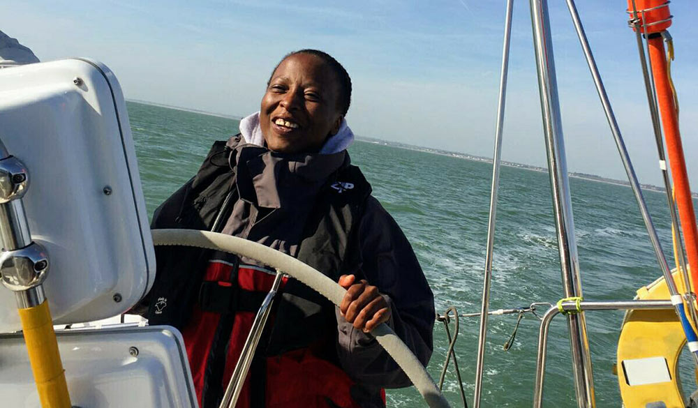 Smiling woman steering yacht on a sunny day, off the coast