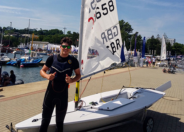 Posed shot of Will Dyson standing in front of his sailing dinghy