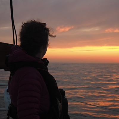 silhouette of sailor looking out at the sunset across the water