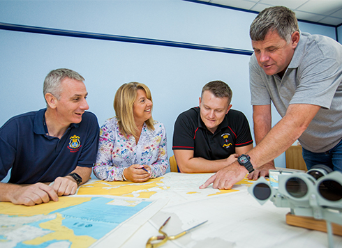 Group of people in classroom listening to instructor pointing at chart